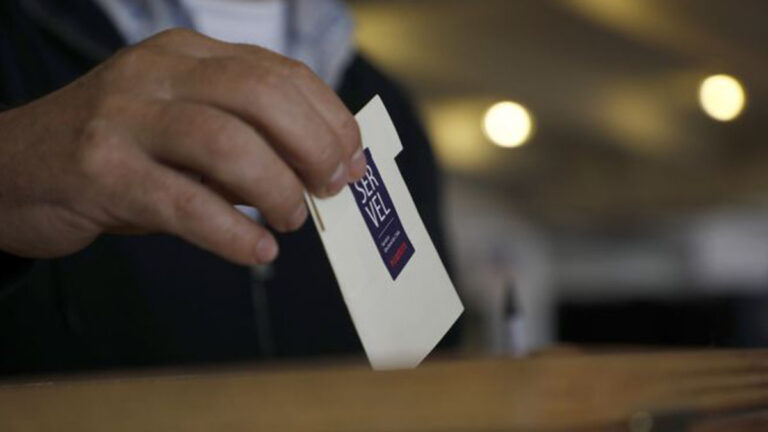 Imagen centrada en una mano que está depositando un voto en la urna voto electoral en la urna