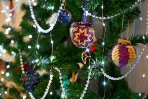 La imagen muestra un árbol de Navidad de plástico verde oscuro decorado con adornos y luces